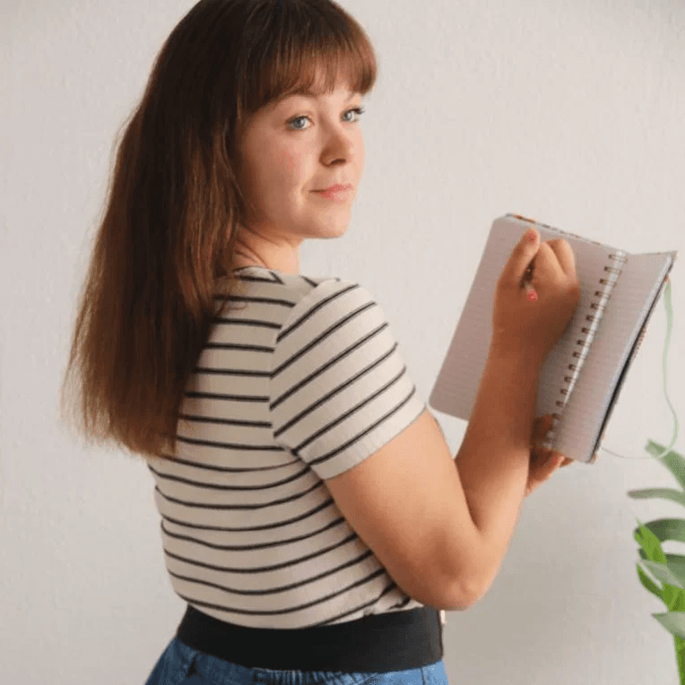 femme écrivant dans un carnet avec un stylo près d'une plante verte